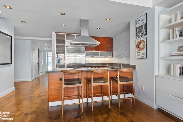 kitchen featuring island exhaust hood, stainless steel built in refrigerator, a sink, modern cabinets, and baseboards