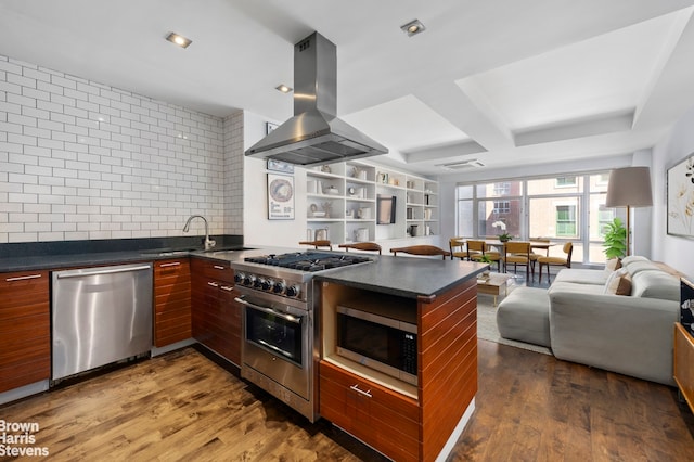 kitchen with appliances with stainless steel finishes, island exhaust hood, dark countertops, and open floor plan