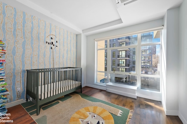 bedroom featuring baseboards, wood finished floors, wallpapered walls, and a crib