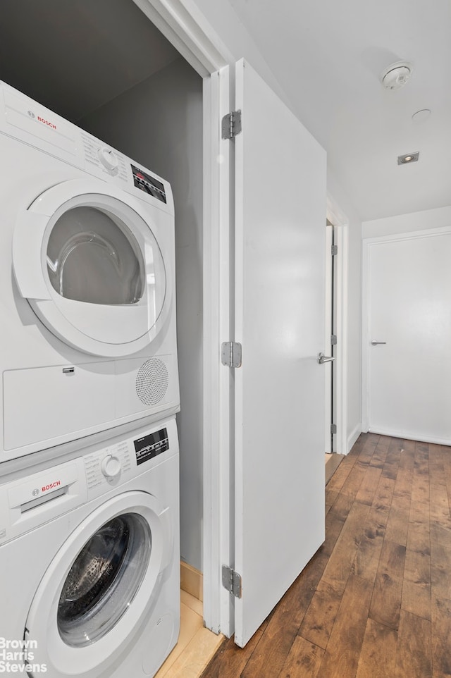 laundry room featuring stacked washing machine and dryer, wood-type flooring, and baseboards