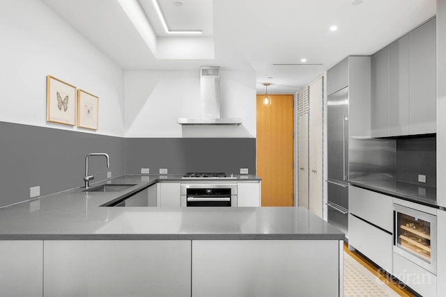 kitchen with wall chimney range hood, oven, a sink, a peninsula, and modern cabinets