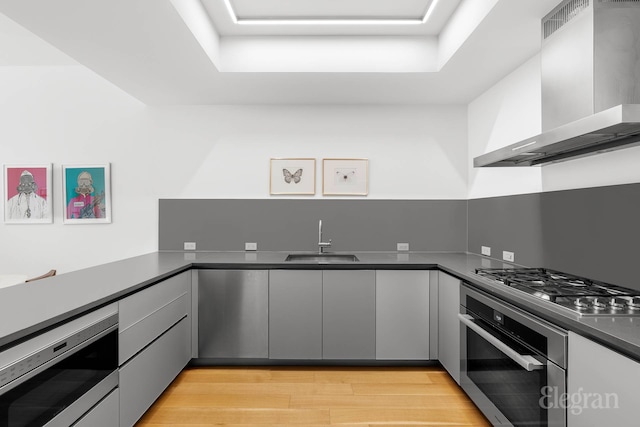 kitchen featuring a sink, dark countertops, stainless steel appliances, light wood-type flooring, and wall chimney exhaust hood