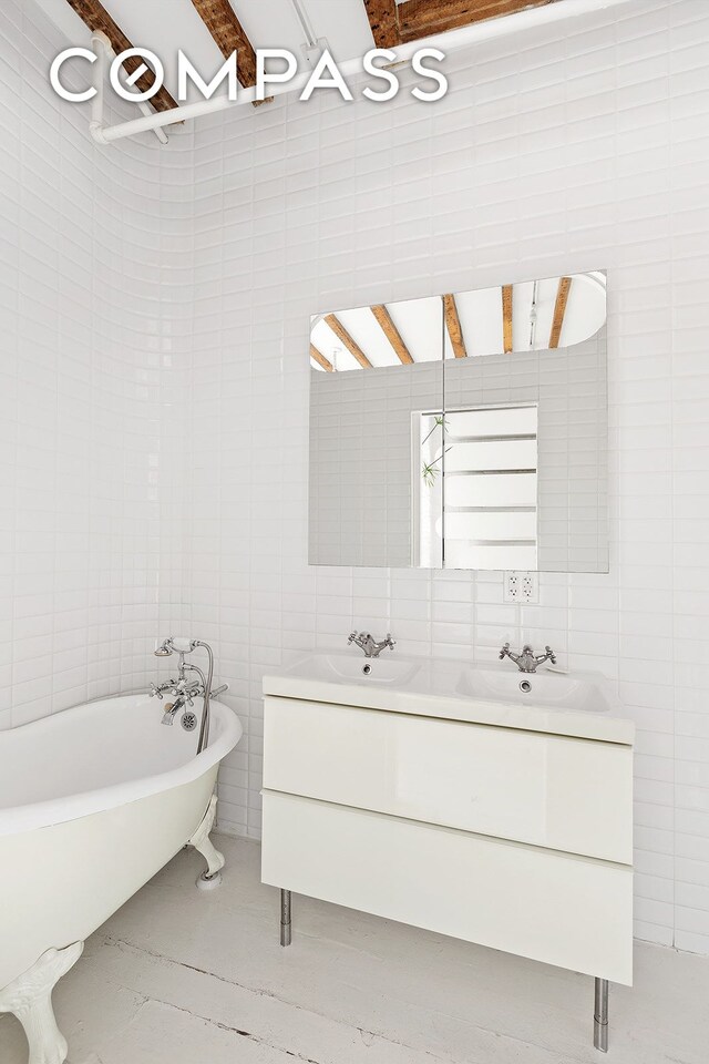 full bath with double vanity, a freestanding tub, tile walls, and a sink