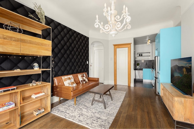 living room featuring arched walkways, dark wood-type flooring, a chandelier, and baseboards