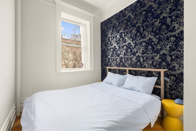 bedroom featuring multiple windows, wallpapered walls, baseboards, and wood finished floors
