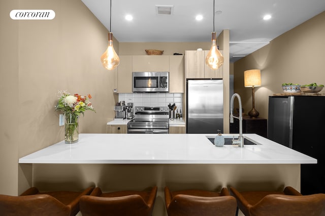 kitchen with appliances with stainless steel finishes, a sink, light countertops, a kitchen breakfast bar, and decorative light fixtures