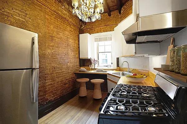kitchen with a sink, freestanding refrigerator, brick wall, gas stove, and extractor fan