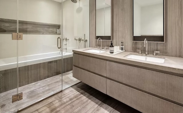 bathroom featuring double vanity, wood finished floors, a stall shower, and a sink