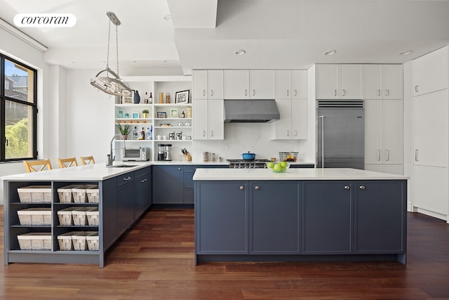 kitchen with a sink, under cabinet range hood, open shelves, a kitchen island, and stainless steel built in refrigerator