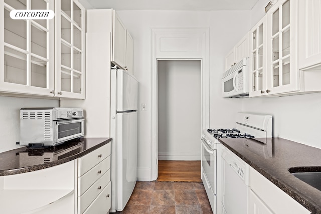 kitchen featuring white appliances, stone finish floors, dark stone countertops, and baseboards