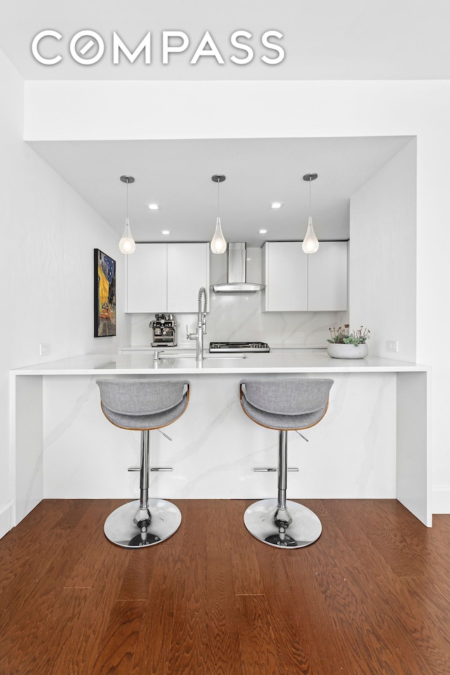 kitchen featuring wall chimney exhaust hood, white cabinets, a kitchen breakfast bar, and modern cabinets