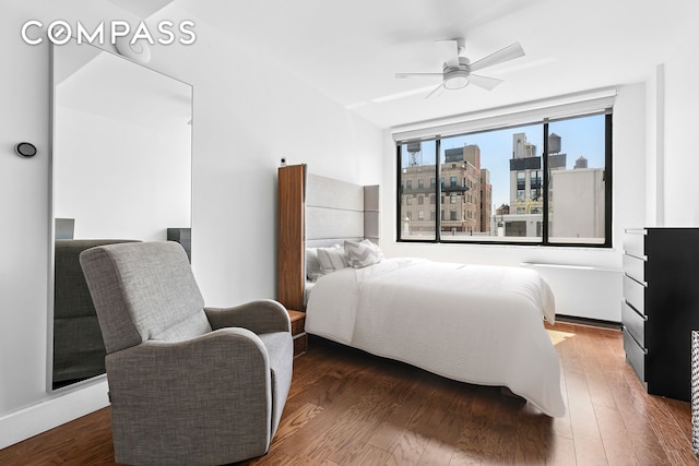 bedroom with wood finished floors, ceiling fan, and a city view