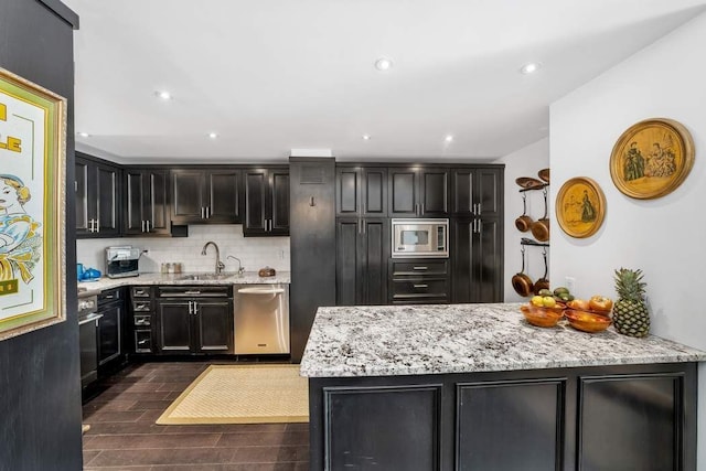 207 E 74th St Unit 7F, New York City, NY 10021 - kitchen with stainless steel appliances, a sink, backsplash, light stone counters, and dark wood-style flooring