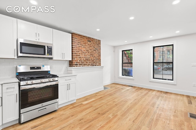 kitchen featuring backsplash, appliances with stainless steel finishes, baseboards, light wood-style floors, and white cabinetry
