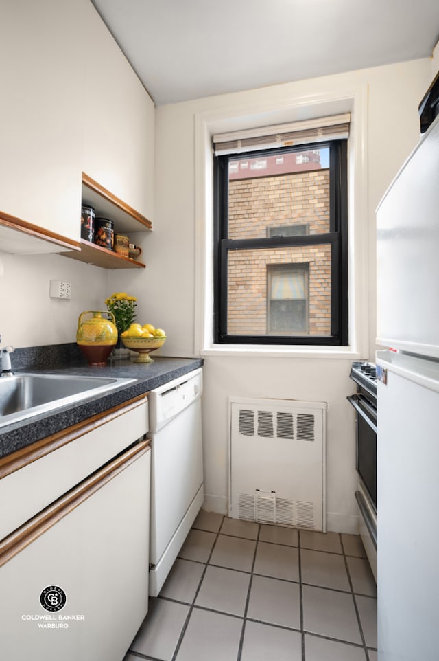 kitchen featuring white appliances, radiator heating unit, white cabinetry, dark countertops, and light tile patterned floors