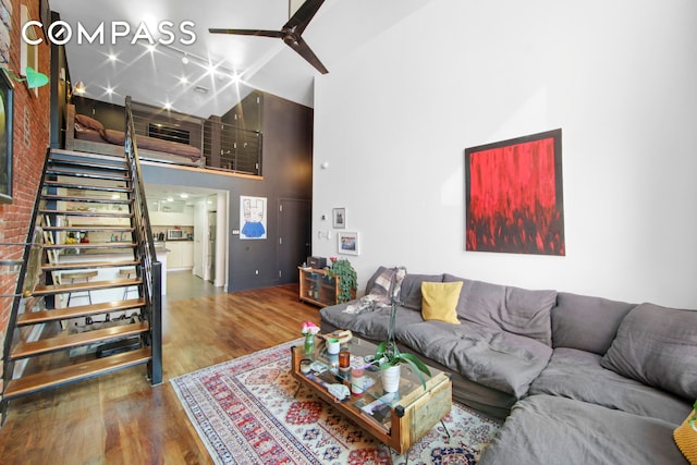 living room with a towering ceiling, wood finished floors, stairs, and ceiling fan