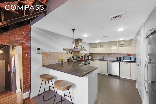 66 N 1st St Unit 1C, New York City, NY 11249 - kitchen with stainless steel appliances, island range hood, a peninsula, dark countertops, and tasteful backsplash