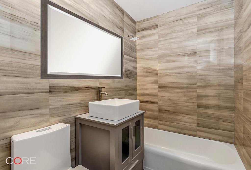 full bath with toilet, tile walls, vanity, and shower / bathing tub combination