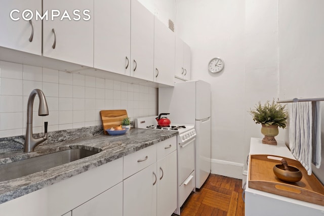 kitchen featuring white gas range oven, a sink, tasteful backsplash, white cabinets, and baseboards