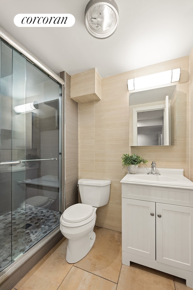 bathroom featuring tile patterned flooring, toilet, vanity, a stall shower, and tile walls