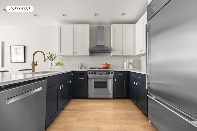 kitchen with high end appliances, wall chimney range hood, white cabinets, light countertops, and light wood-type flooring