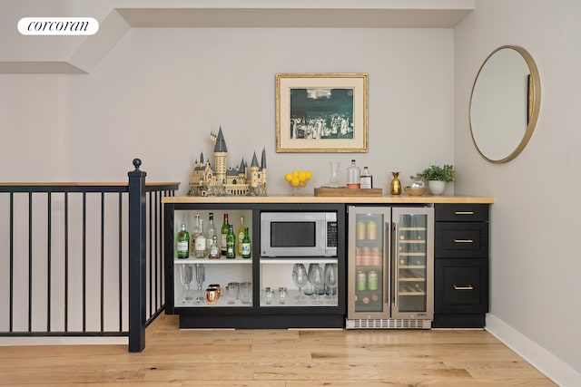 indoor dry bar featuring wine cooler, stainless steel microwave, wood finished floors, and baseboards