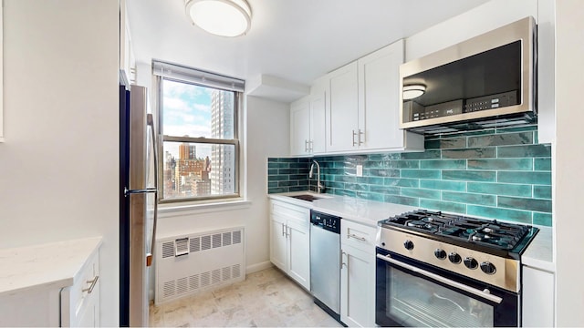 kitchen featuring appliances with stainless steel finishes, radiator, a sink, backsplash, and white cabinetry