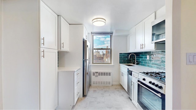 kitchen with radiator heating unit, stainless steel appliances, a sink, white cabinets, and tasteful backsplash