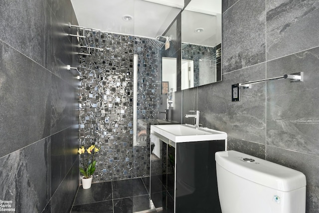bathroom with a tile shower, toilet, vanity, and tile walls