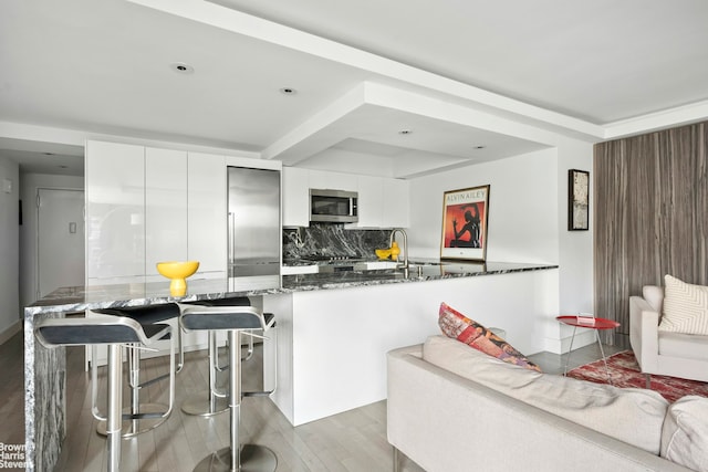 kitchen featuring stainless steel appliances, dark stone countertops, decorative backsplash, white cabinetry, and modern cabinets