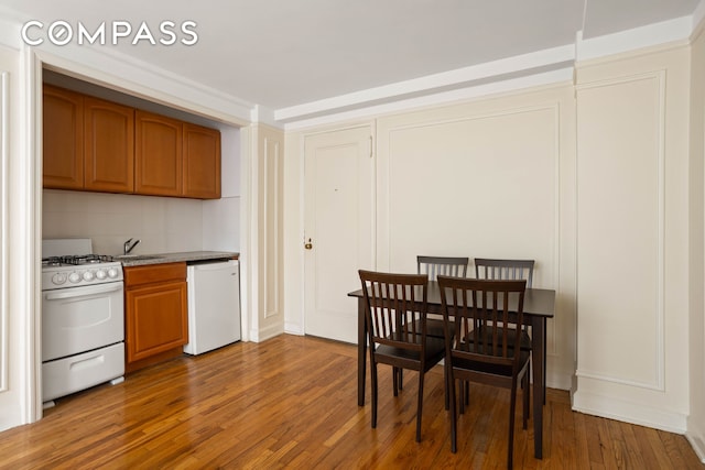 kitchen with white appliances, brown cabinets, a sink, and wood finished floors