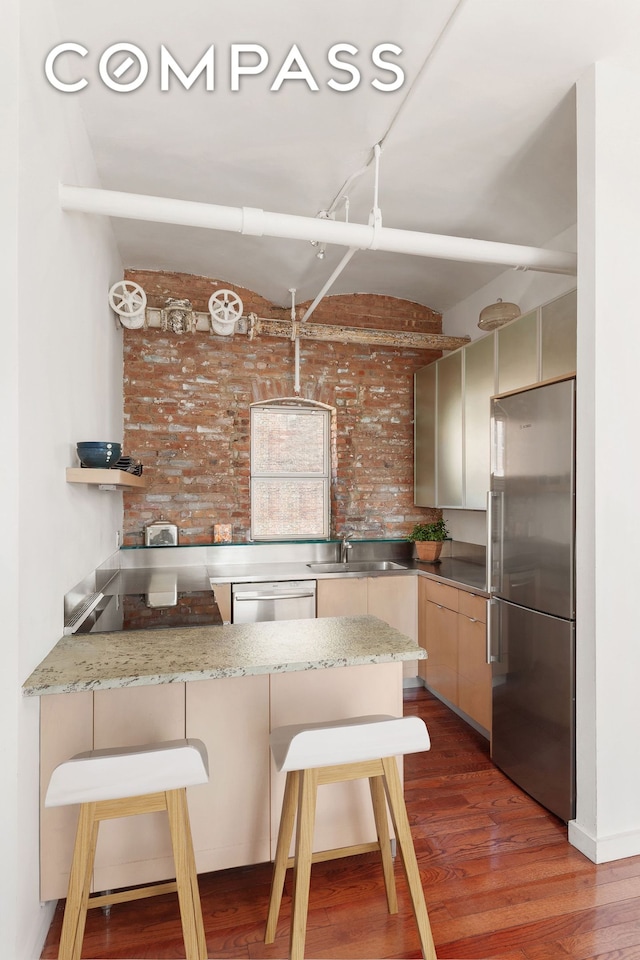 543 Broadway Ph Ph, New York City, NY 10012 - kitchen with appliances with stainless steel finishes, brick wall, a sink, a kitchen bar, and wood finished floors