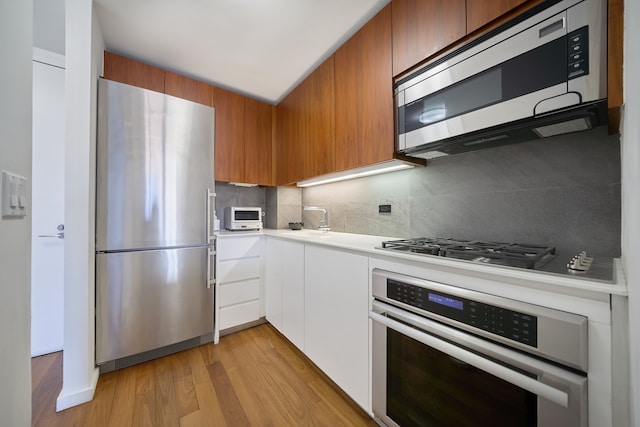 kitchen featuring stainless steel appliances, backsplash, light countertops, a sink, and light wood-style flooring