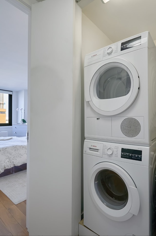 clothes washing area with stacked washer / drying machine and wood finished floors