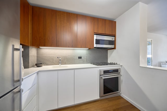kitchen with stainless steel appliances, a sink, backsplash, and light countertops