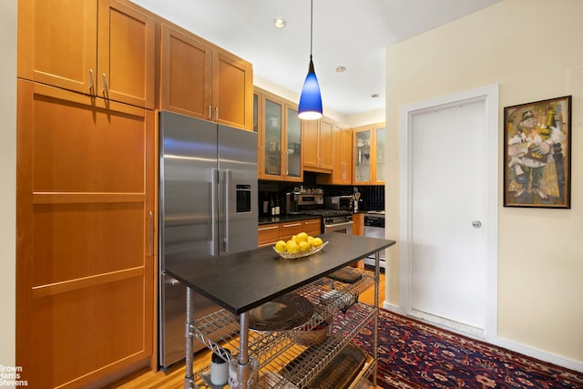 kitchen featuring premium appliances, dark countertops, tasteful backsplash, glass insert cabinets, and pendant lighting