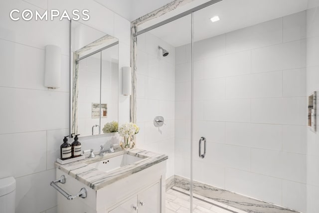 bathroom with a shower stall, toilet, vanity, and tile walls