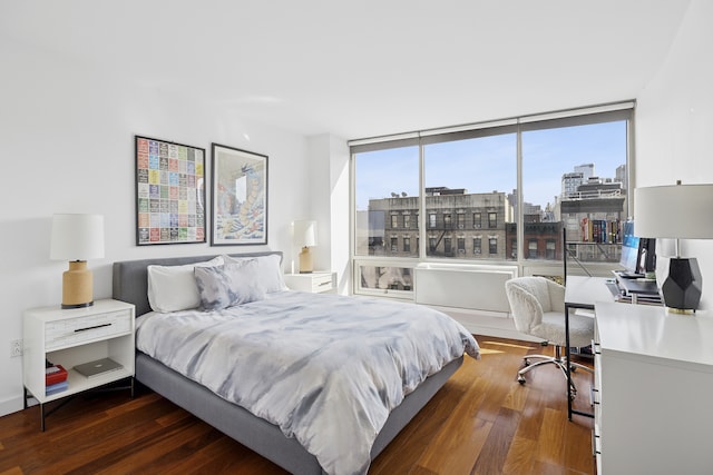bedroom with dark wood-style flooring, an office area, and a city view