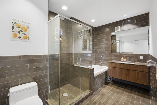 bathroom featuring tile walls, a stall shower, vanity, a garden tub, and toilet