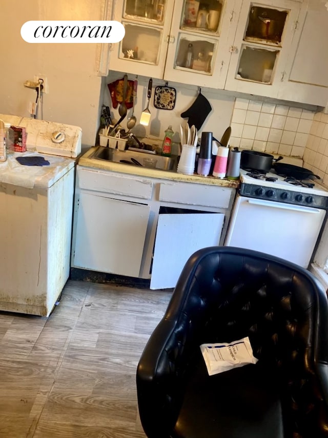 kitchen featuring glass insert cabinets, washer / clothes dryer, white cabinetry, a sink, and backsplash