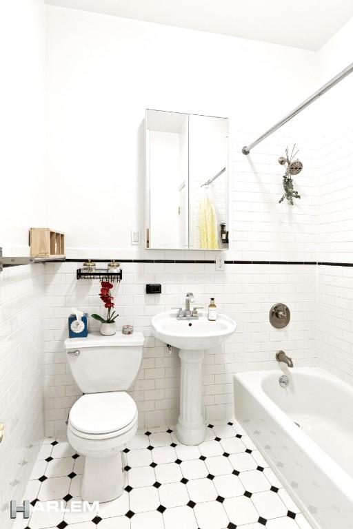 bathroom featuring tile walls, a wainscoted wall, toilet, and a sink