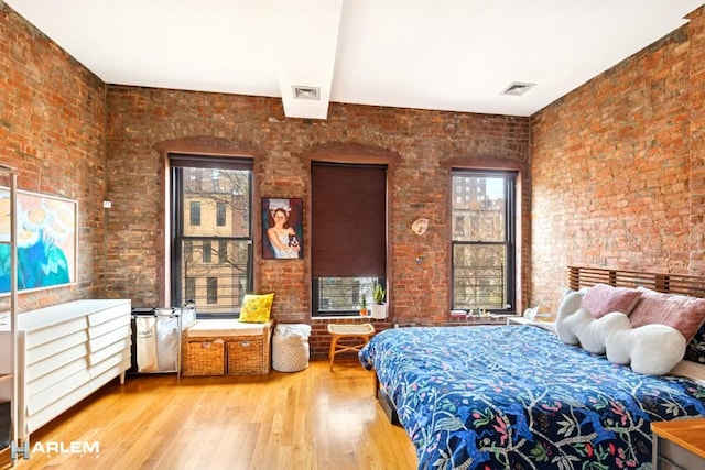 bedroom with wood finished floors, brick wall, visible vents, and multiple windows