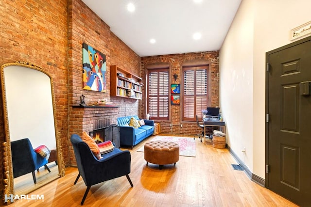 sitting room with baseboards, brick wall, recessed lighting, a fireplace, and wood finished floors