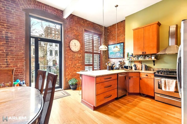 kitchen with brick wall, a peninsula, appliances with stainless steel finishes, and light wood finished floors