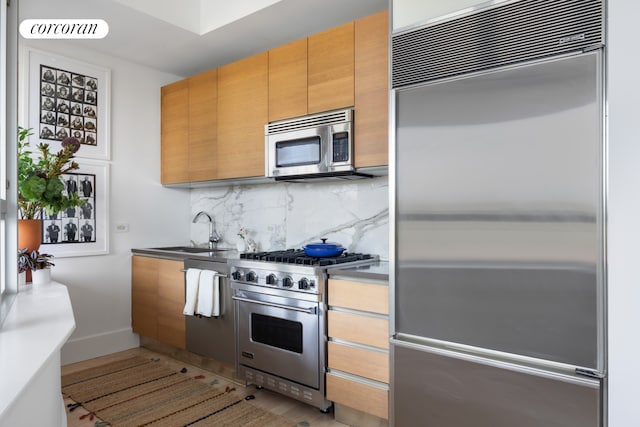 kitchen with a sink, baseboards, tasteful backsplash, premium appliances, and visible vents