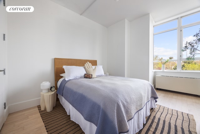 bedroom with light wood-type flooring, baseboards, radiator heating unit, and multiple windows