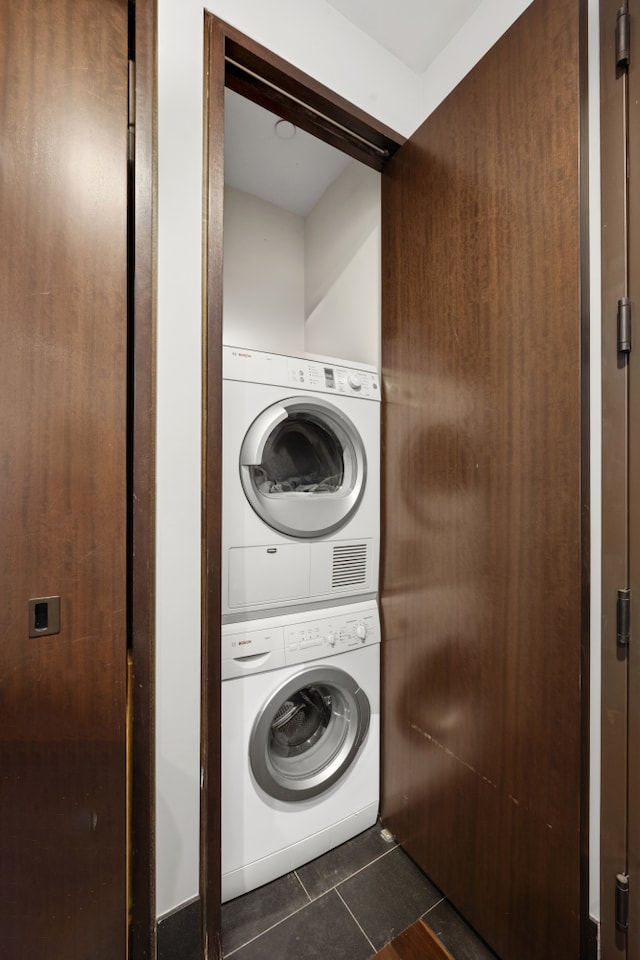 laundry area with dark tile patterned floors, stacked washer and dryer, and laundry area