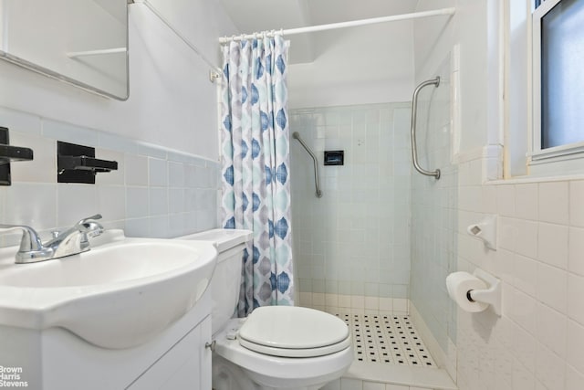 full bathroom featuring tile walls, a tile shower, toilet, vanity, and a wainscoted wall