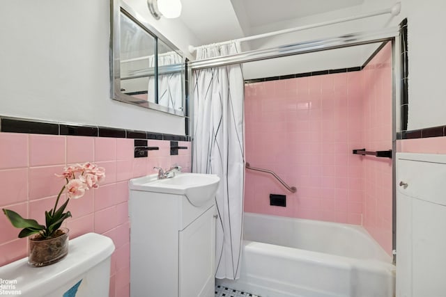 bathroom with tile walls, shower / bath combo with shower curtain, vanity, toilet, and a wainscoted wall