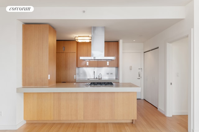 450 W 17th St Unit 2408, New York City, NY 10011 - kitchen with wall chimney range hood, light wood-style flooring, light countertops, a peninsula, and modern cabinets
